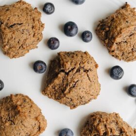 Five cookies on a white plate with fresh blueberries scattered around them.