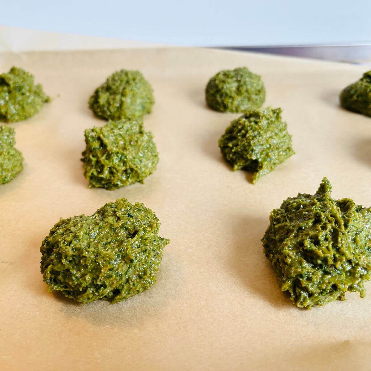 Green cookie dough balls on a sheet pan lined with parchment paper.