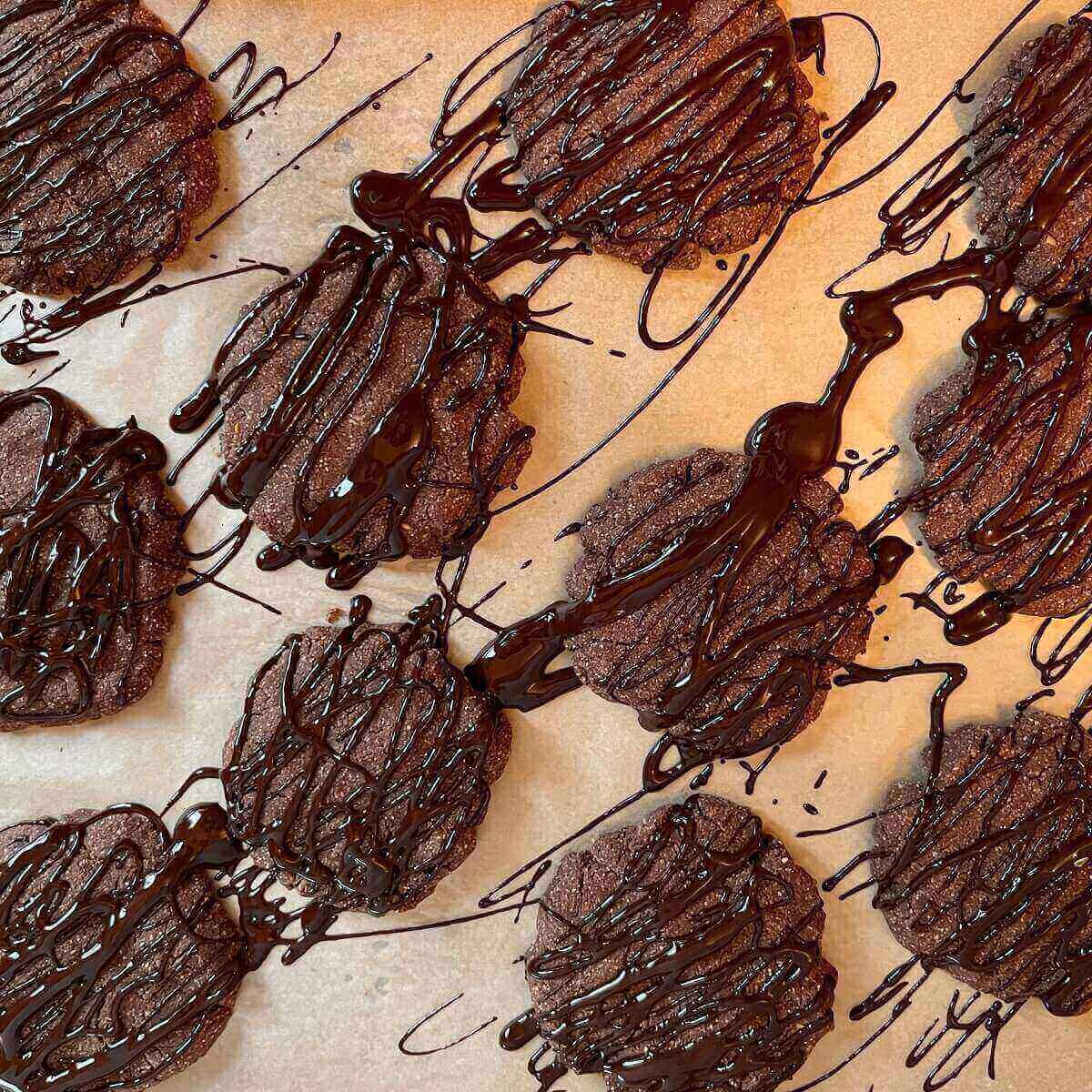 Cookies on parchment paper with melted chocolate drizzled on top.