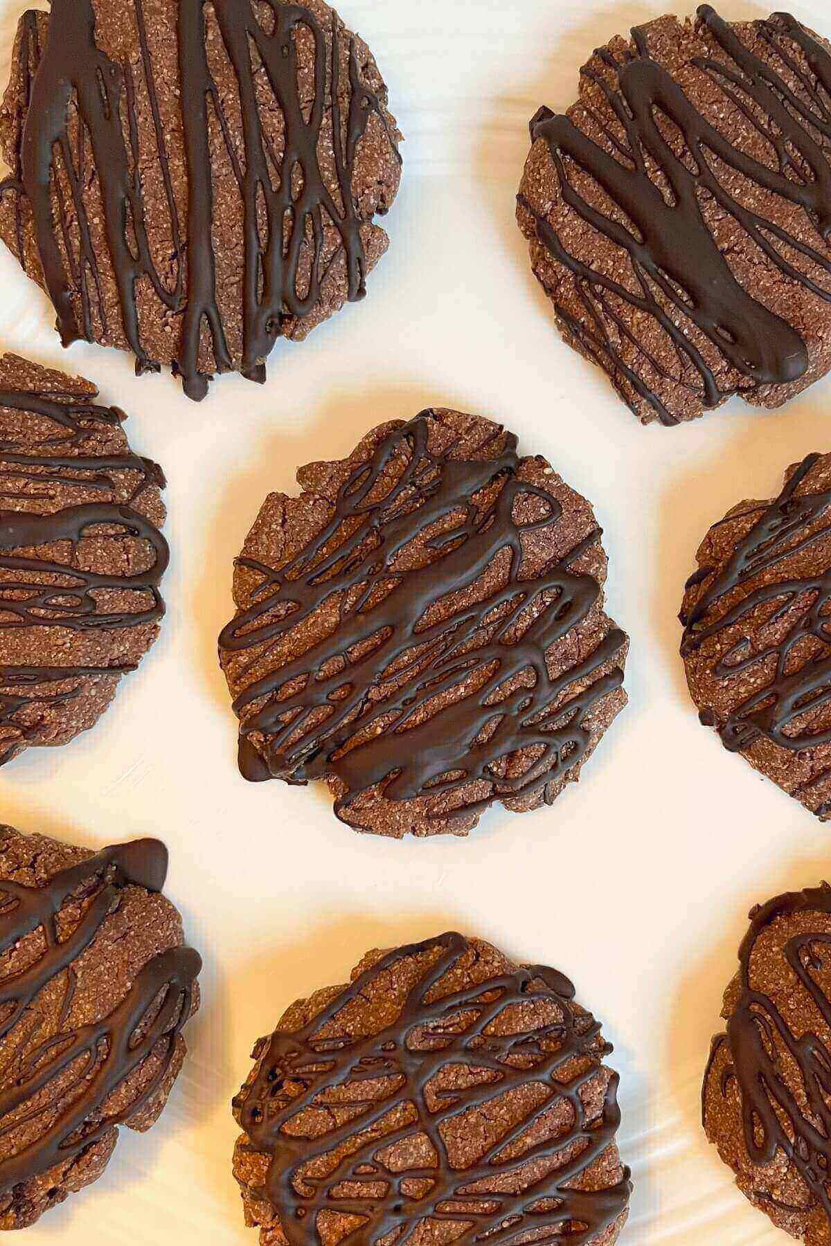 Brown cookies drizzled with dark chocolate on a white plate.