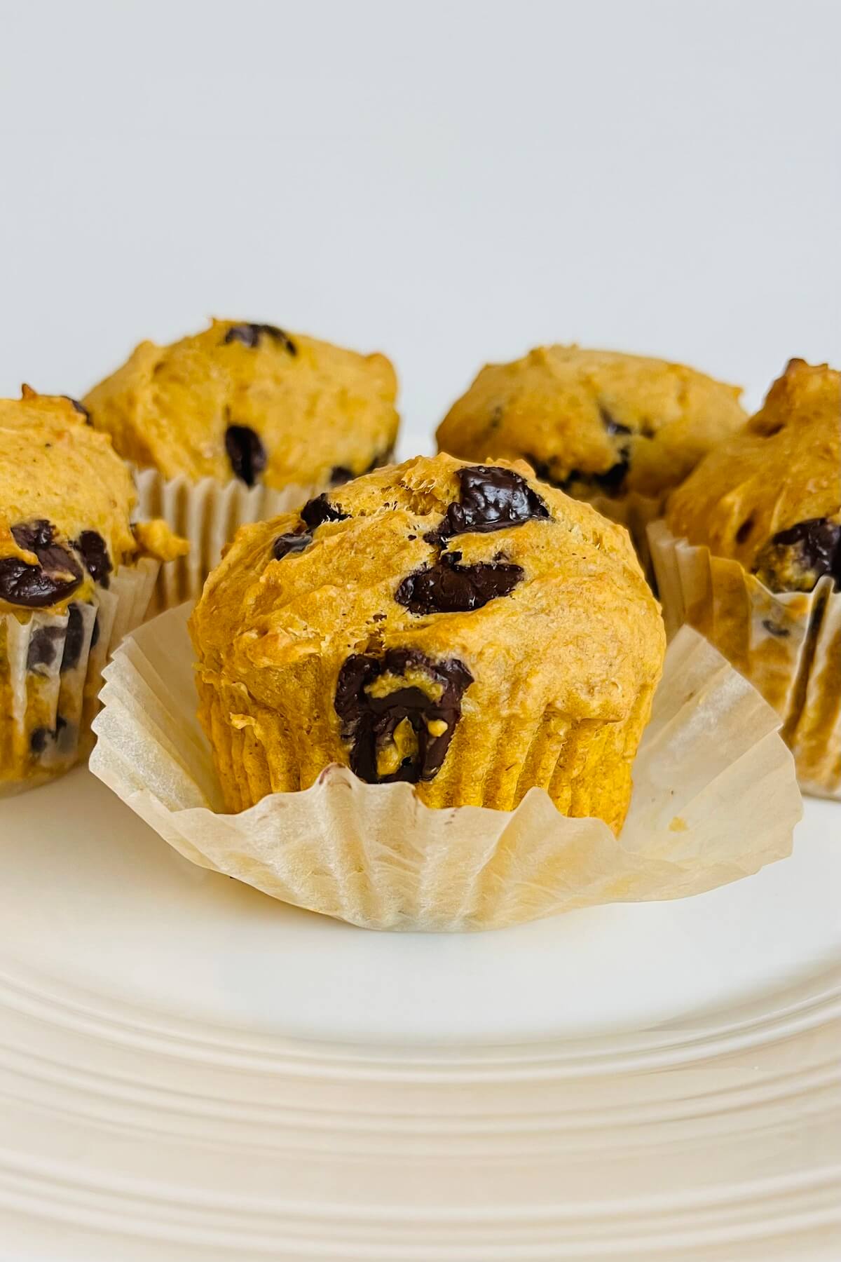 Muffins on a white plate with the paper baking cup peeled off one of them.