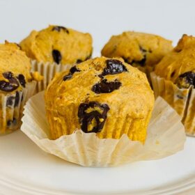 Five muffins on a white plate with the paper liner peeled off one.