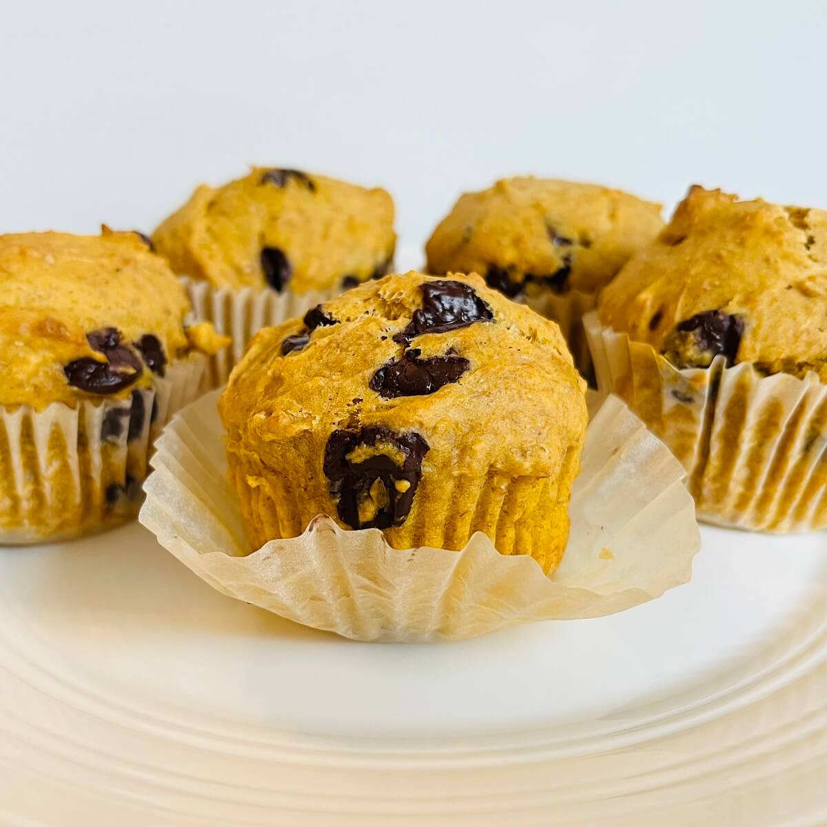 Five vegan sweet potato muffins on a white plate.