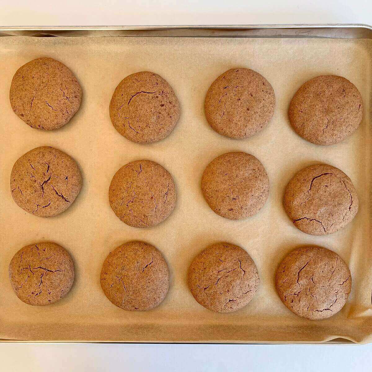 Twelve beige cookies on a sheet pan lined with parchment paper.
