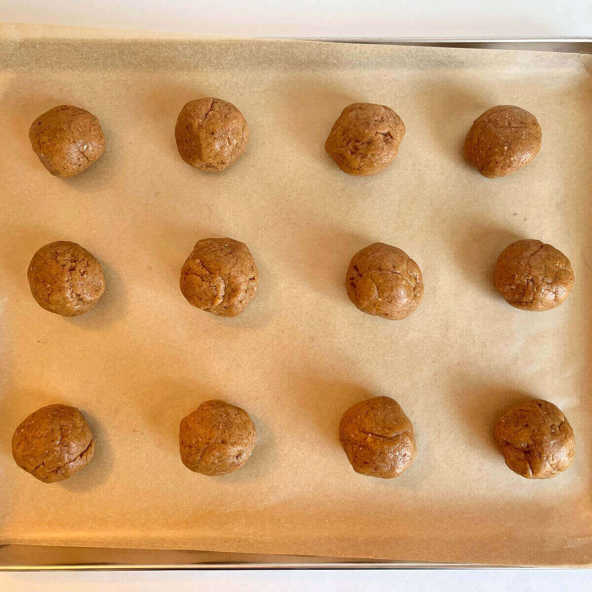 Peanut butter cookie dough balls on a sheet pan lined with parchment paper.