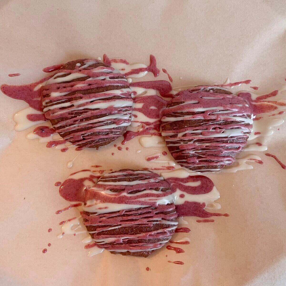 Three cookies drizzled with pink and white chocolate.