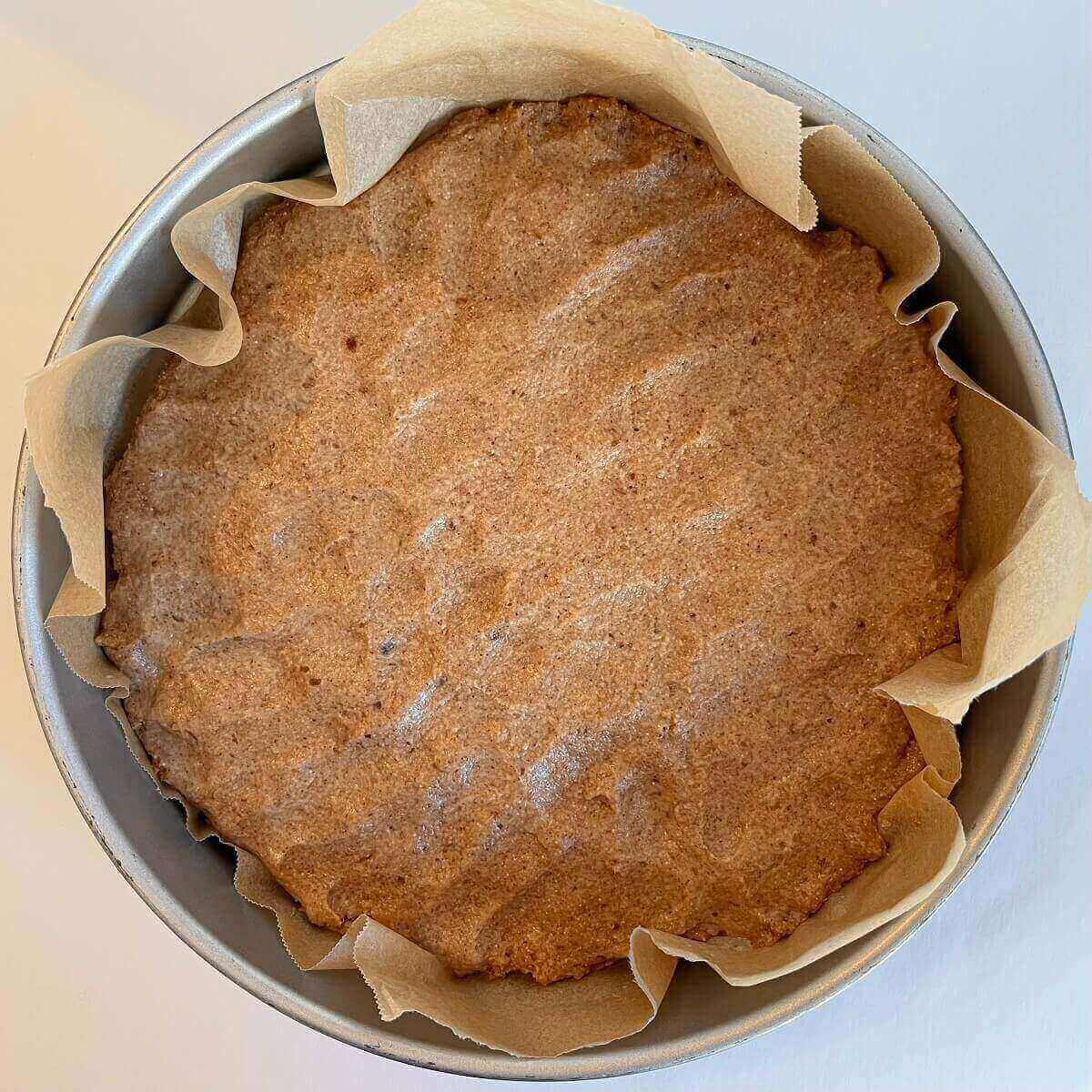 Raw spelt batter in a round baking pan lined with parchment paper.