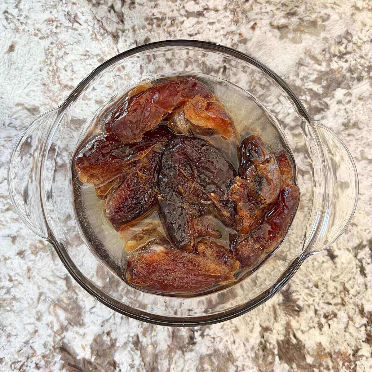 Medjool dates soaking in water in a glass bowl.