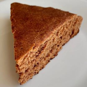 A slice of light brown cake on a white plate.