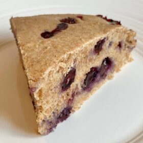A slice of whole wheat blueberry cake on a white plate.