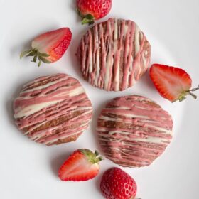 Three vegan strawberry cookies on a plate with some strawberry halves.