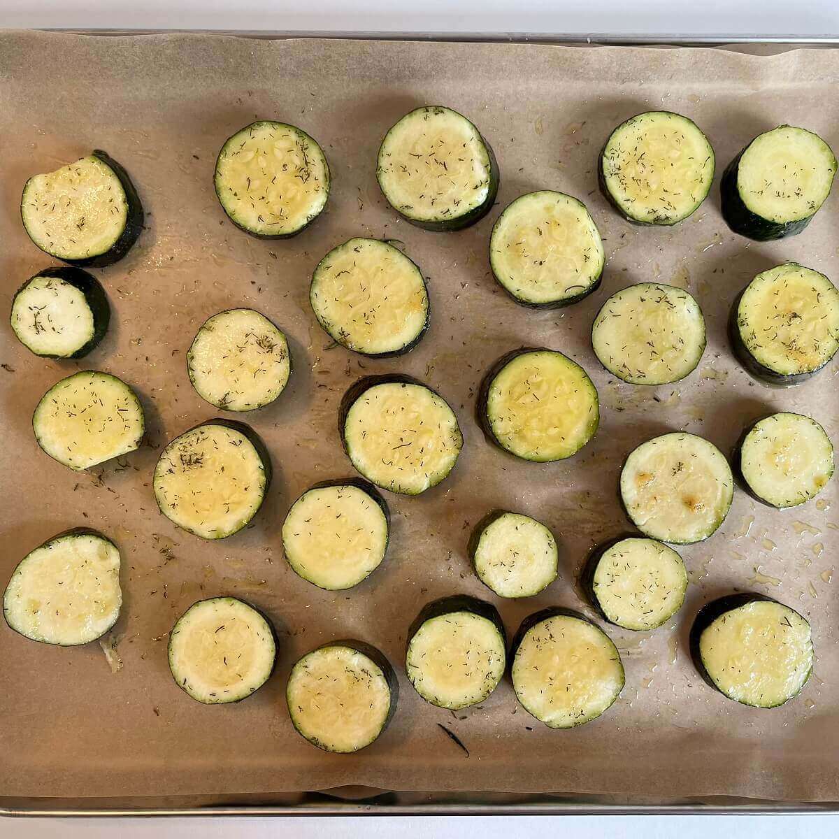 Raw zucchini round slices on a sheet pan lined with parchment paper.