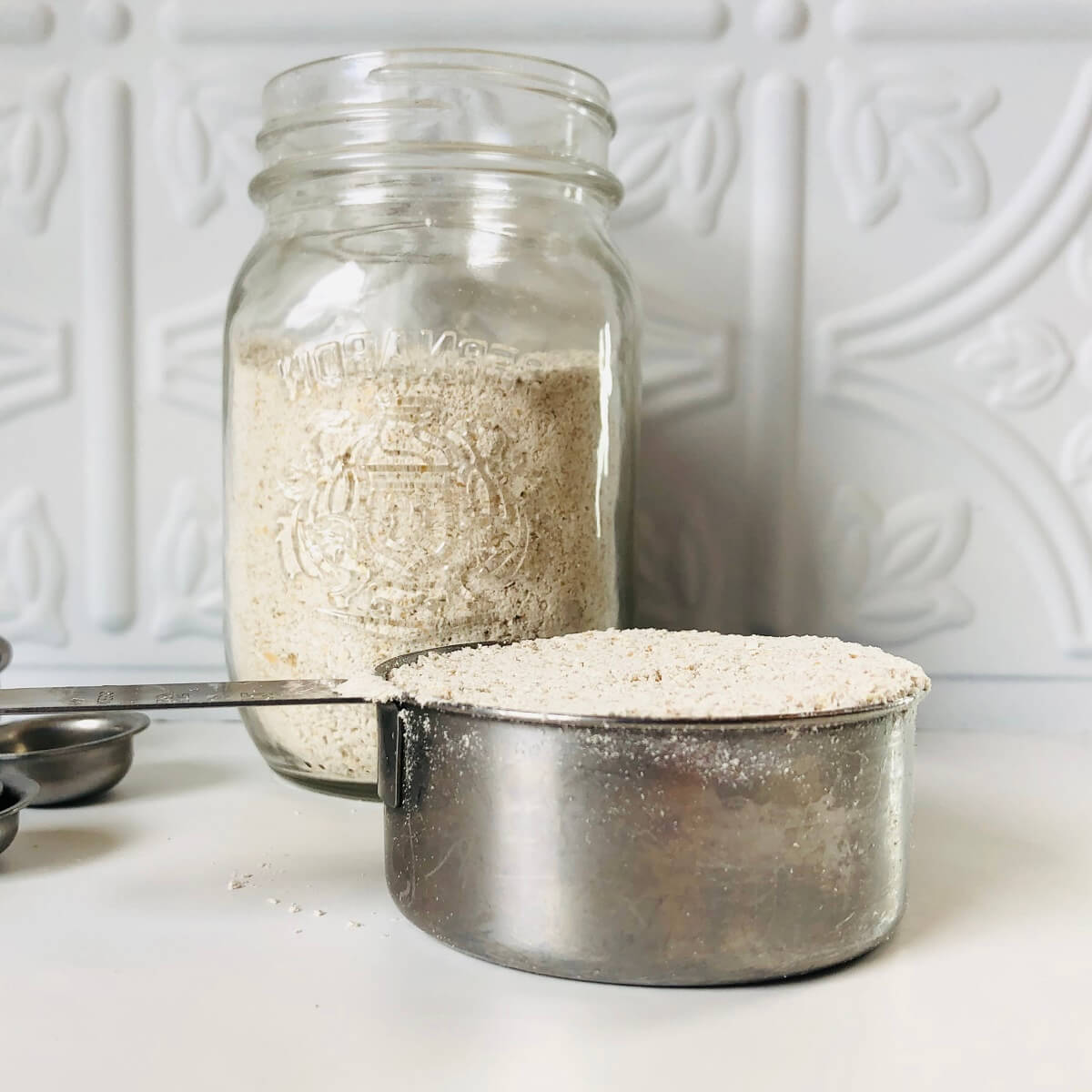 Oat flour in a measuring cup in front of a glass mason jar filled with oat flour.