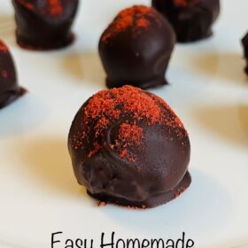 Chocolate truffles dusted with freeze-dried strawberry powder on a white plate.