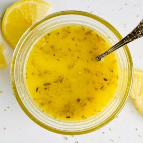 A bowl of lemon salad dressing next to some lemon slices.