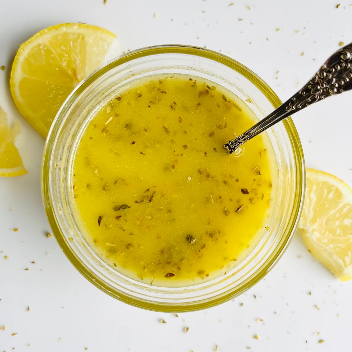 A glass bowl filled with lemon oregano vinaigrette with an antique silver spoon.