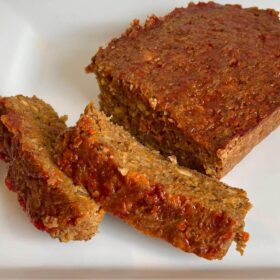 Vegan meatloaf on a white platter with two slices cut off.