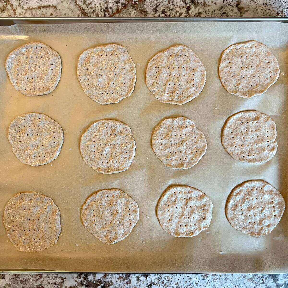 Raw spelt flour crackers on a sheet pan lined with parchment paper.
