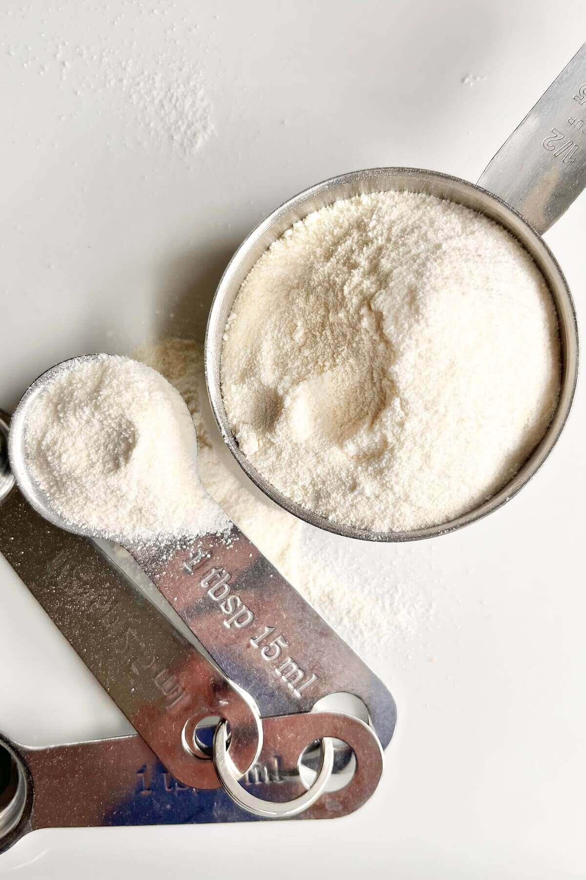 A measuring cup and measuring spoon filled with coconut flour.