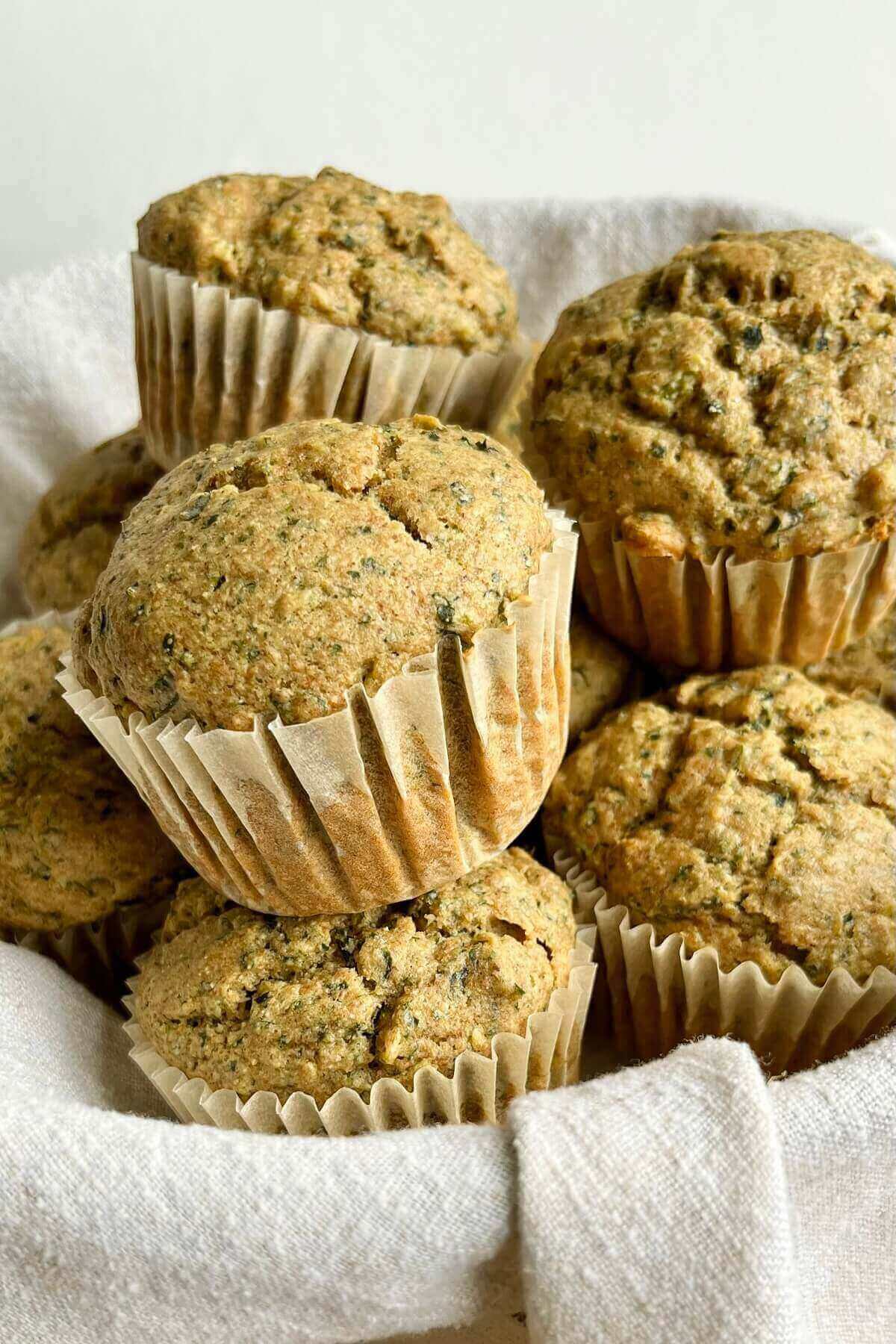 A pile of green-flecked muffins in a basket lined with a linen napkin.