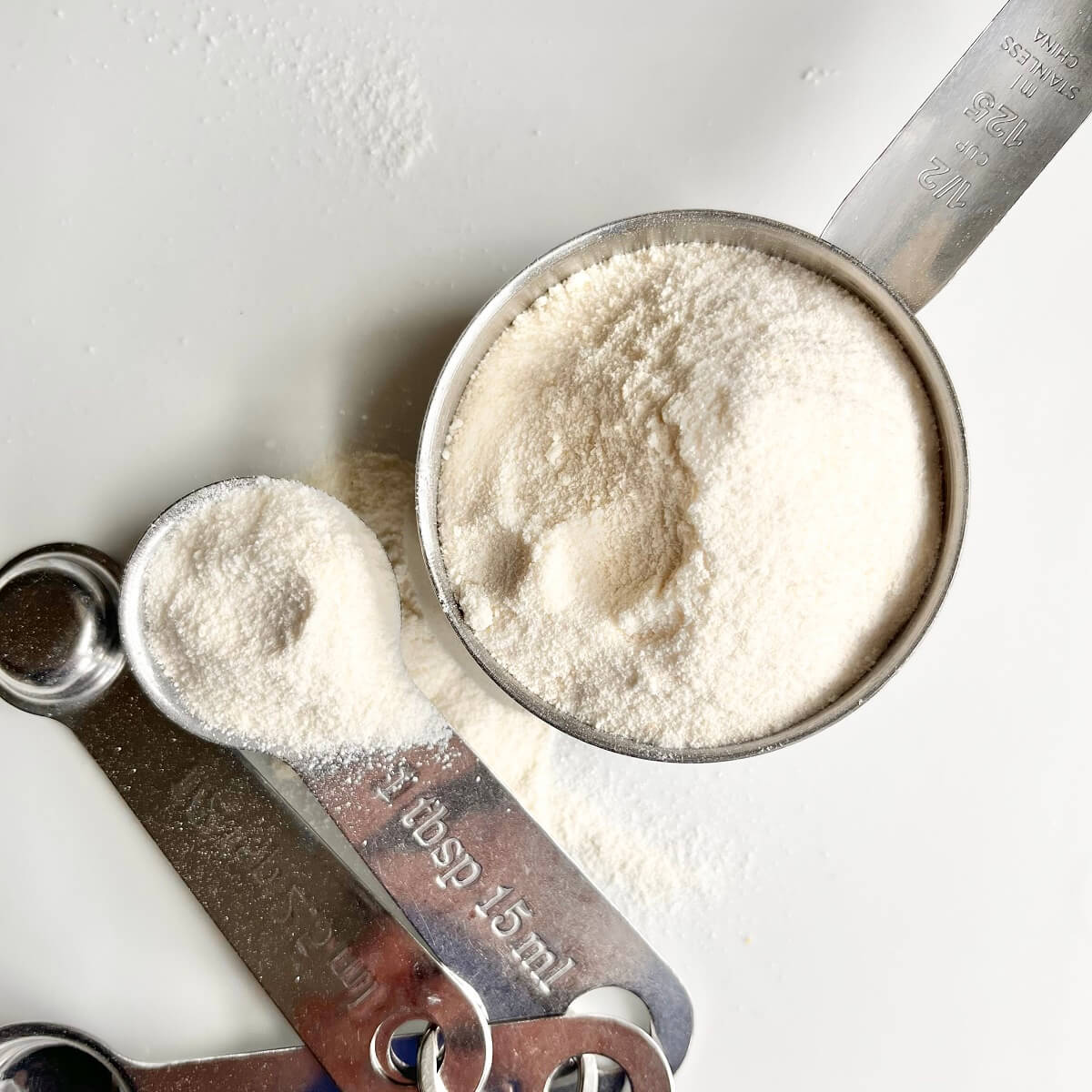 Coconut flour in a metal measuring cup next to measuring spoons.