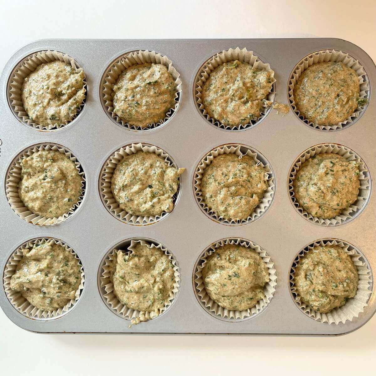 Raw green-flecked muffins in a metal pan.