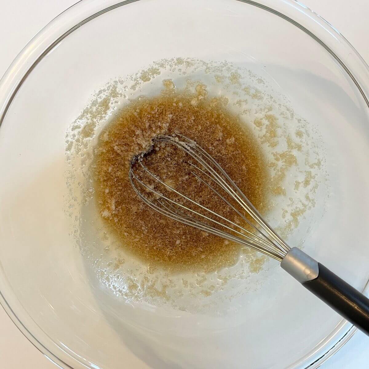 Coconut oil, maple syrup, vanilla extract, and salt mixed together in a glass bowl with a whisk.