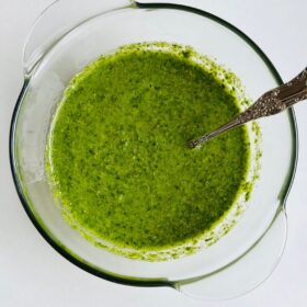 A bowl of green sauce with an antique spoon.