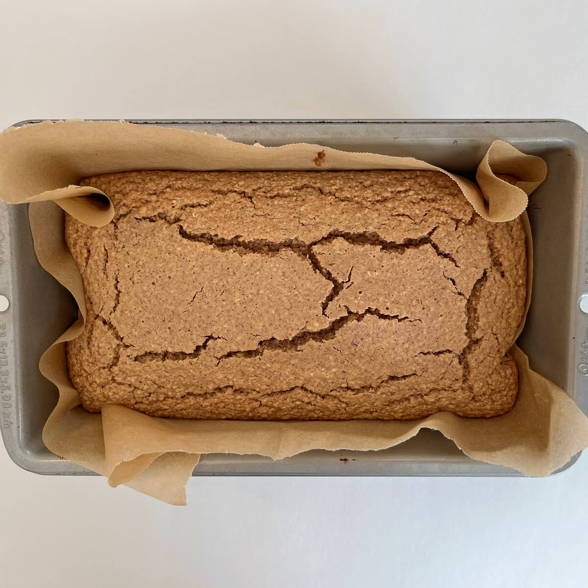 Freshly baked oat cake in a loaf pan lined with parchment paper.