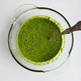 A green lemon herb sauce in a glass bowl with an antique silver spoon.