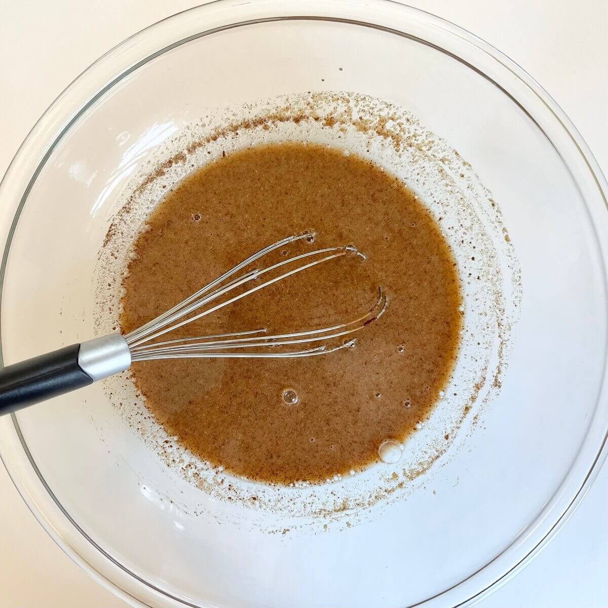 Almond butter, plant-based milk, maple syrup, vanilla, and salt being whisked in a glass bowl.