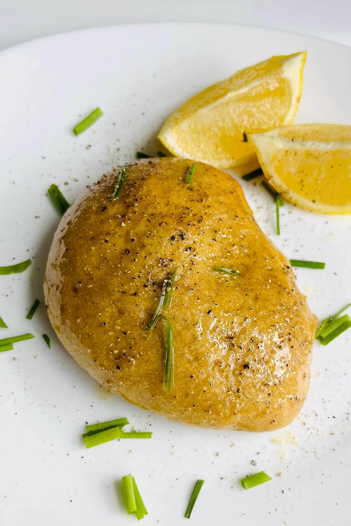 A piece of plant-based chicken on a white plate with lemon wedges.