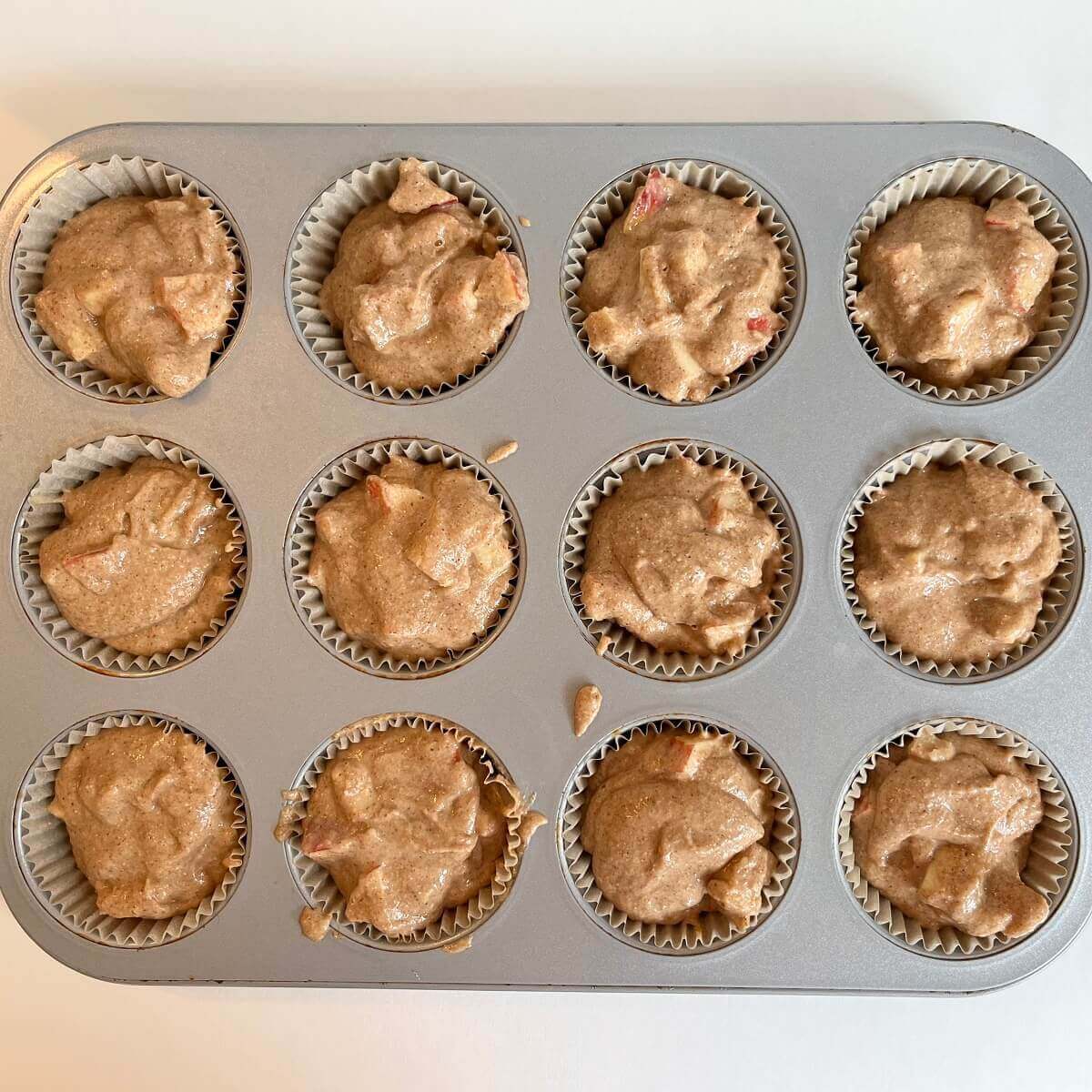 Raw apple muffins in a metal baking pan.