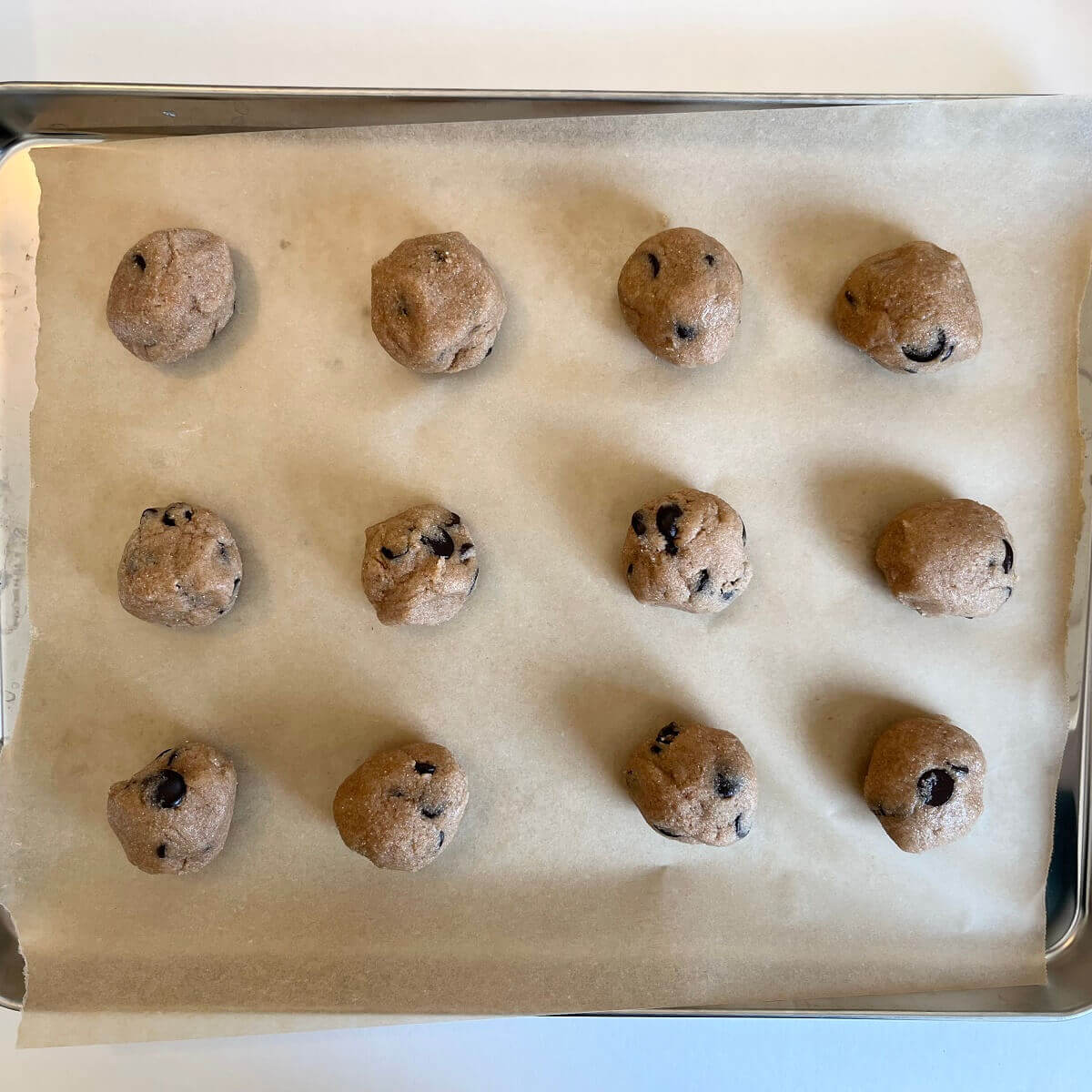 Raw chocolate chip cookie dough balls on a baking sheet lined with parchment paper.