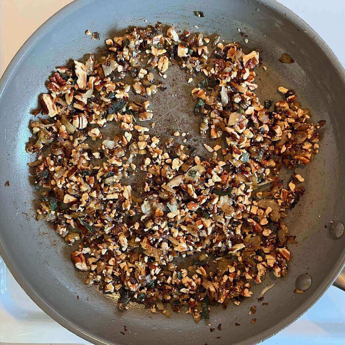 Sauteed onions, chopped pecans, and sage in a frying pan.