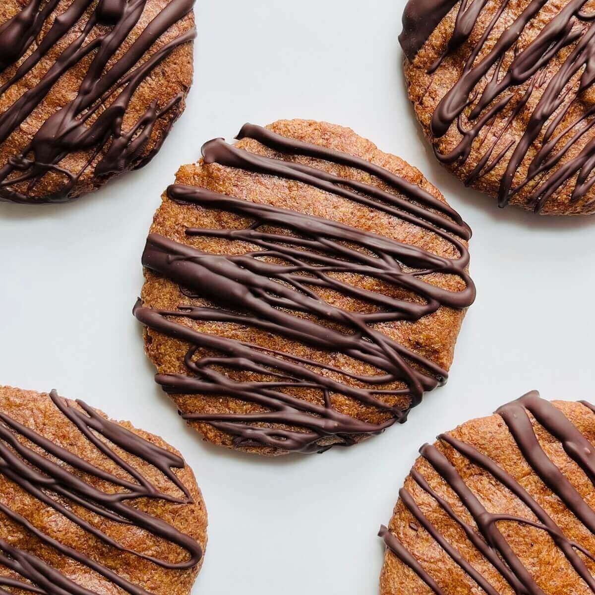 Light brown date-sweetened cookies drizzled with dark chocolate on a white platter.