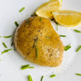 A piece of vegan roasted chicken sprinkled with chives on a plate with lemon wedges.
