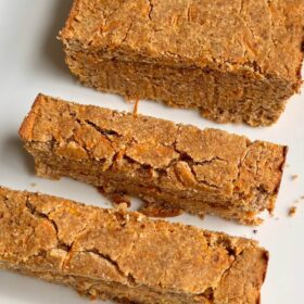 A loaf of carrot cake on a white plate with two slices cut.