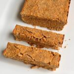 A loaf of coconut flour carrot cake on a white platter with two thick slices cut.