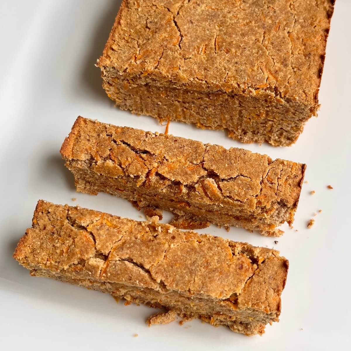 A loaf of coconut flour carrot cake on a white platter with two thick slices cut.