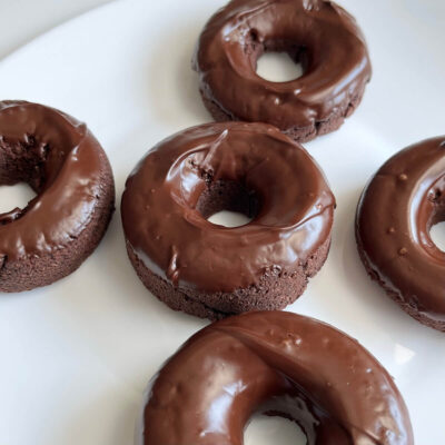 Five chocolate glazed coconut flour donuts on a white plate.