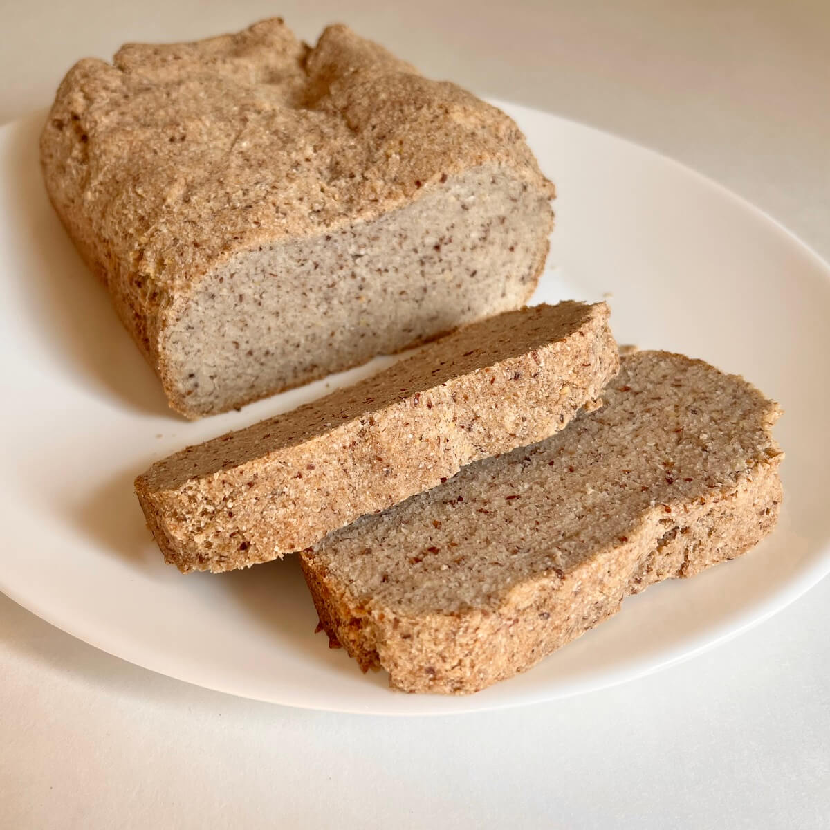 A loaf of flourless bread with two slices cut on a white plate.