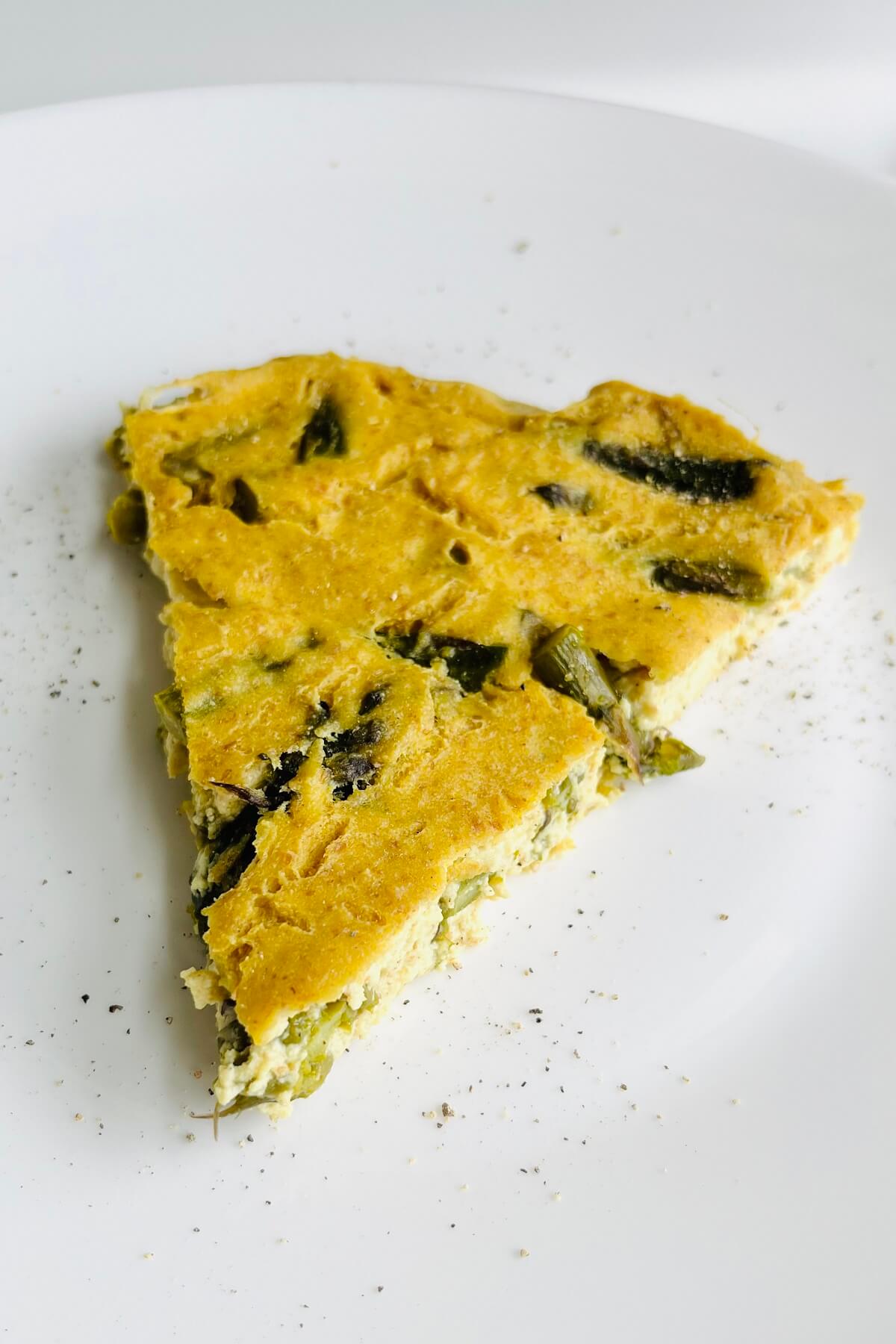 A slice of asparagus frittata on a white plate.