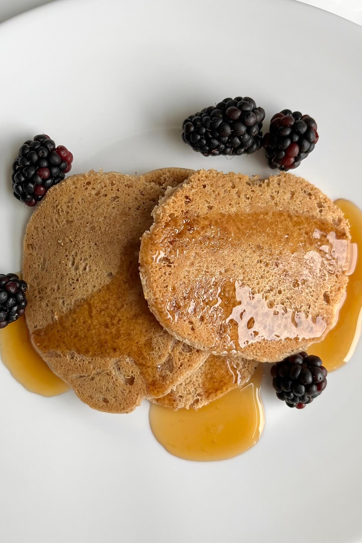 Three pancakes drizzled with syrup on a plate with blackberries.