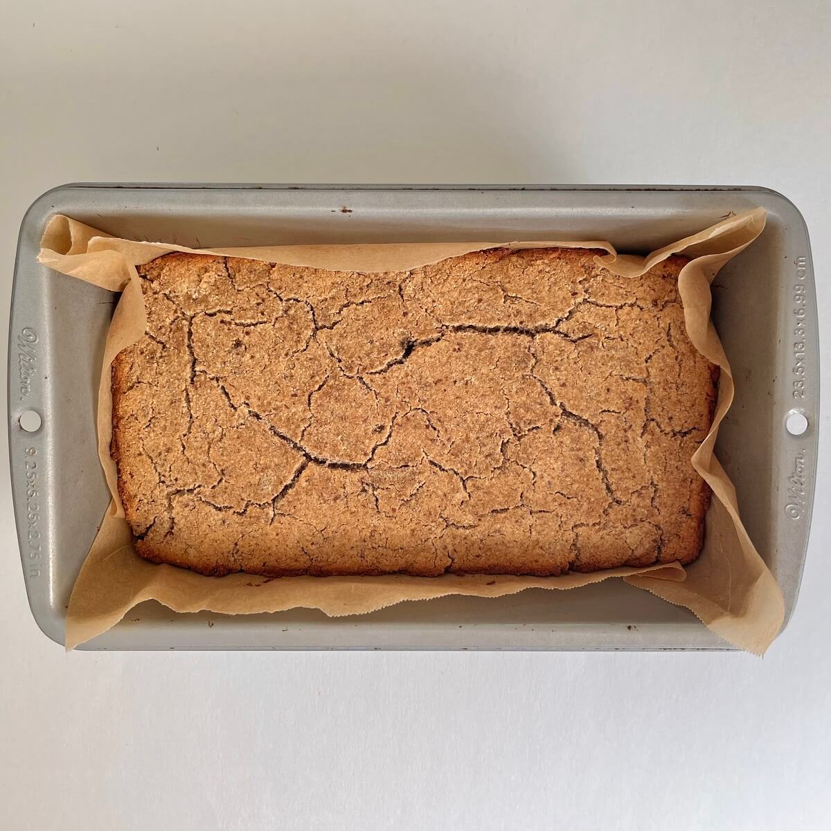 A loaf of freshly baked banana bread in a metal pan lined with parchment paper.