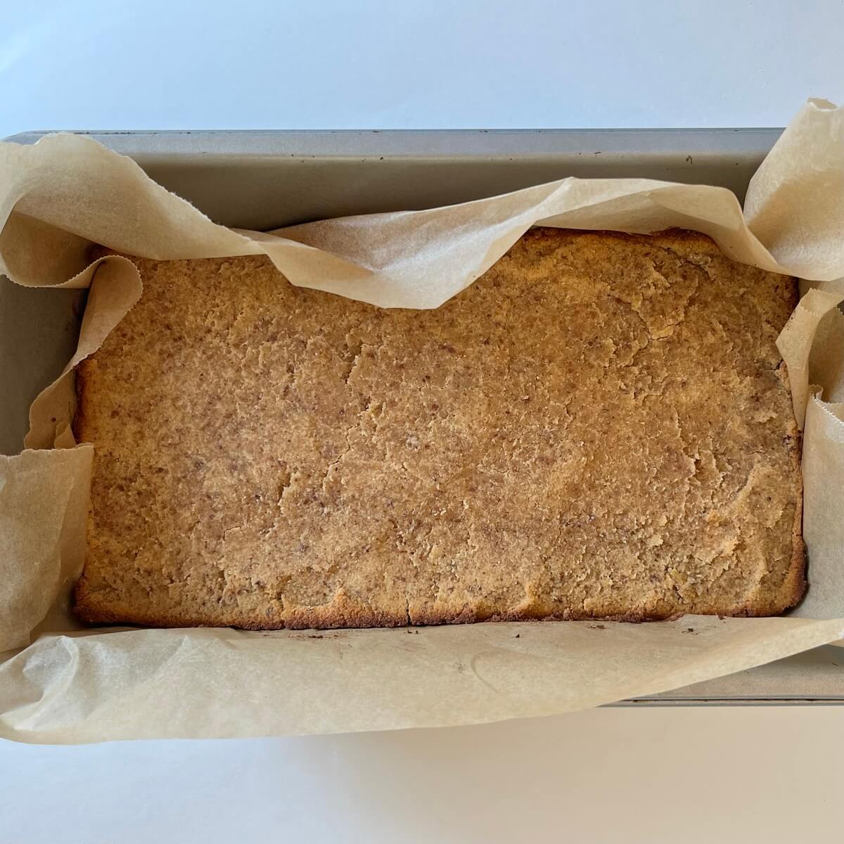 A loaf of lemon cake in a metal pan lined with parchment paper.