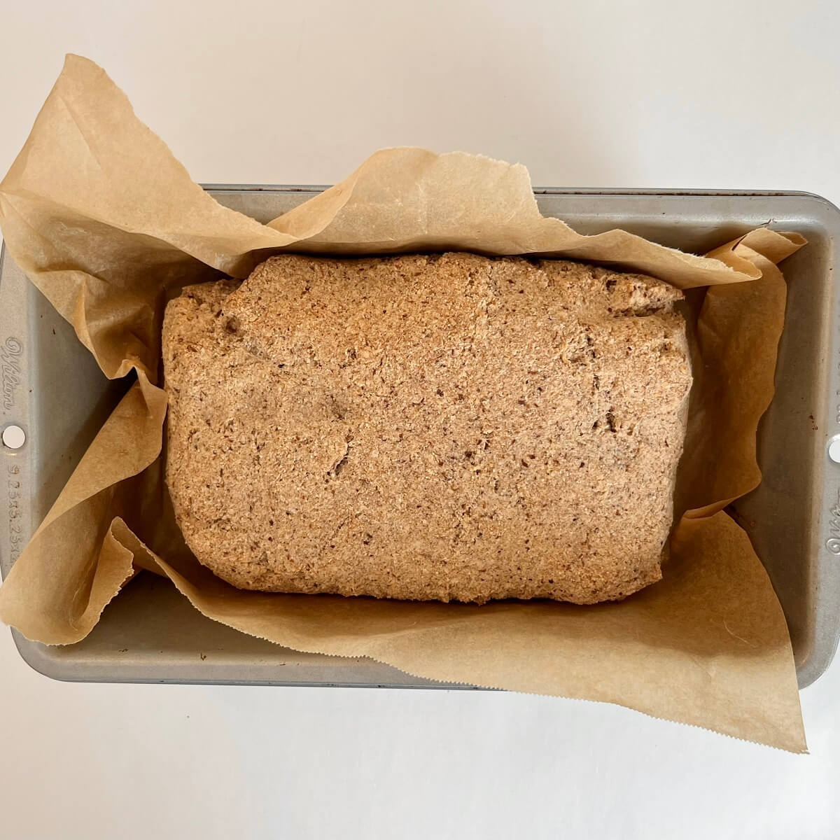 A freshly baked loaf of low-carb bread in a metal loaf pan lined with parchment paper.