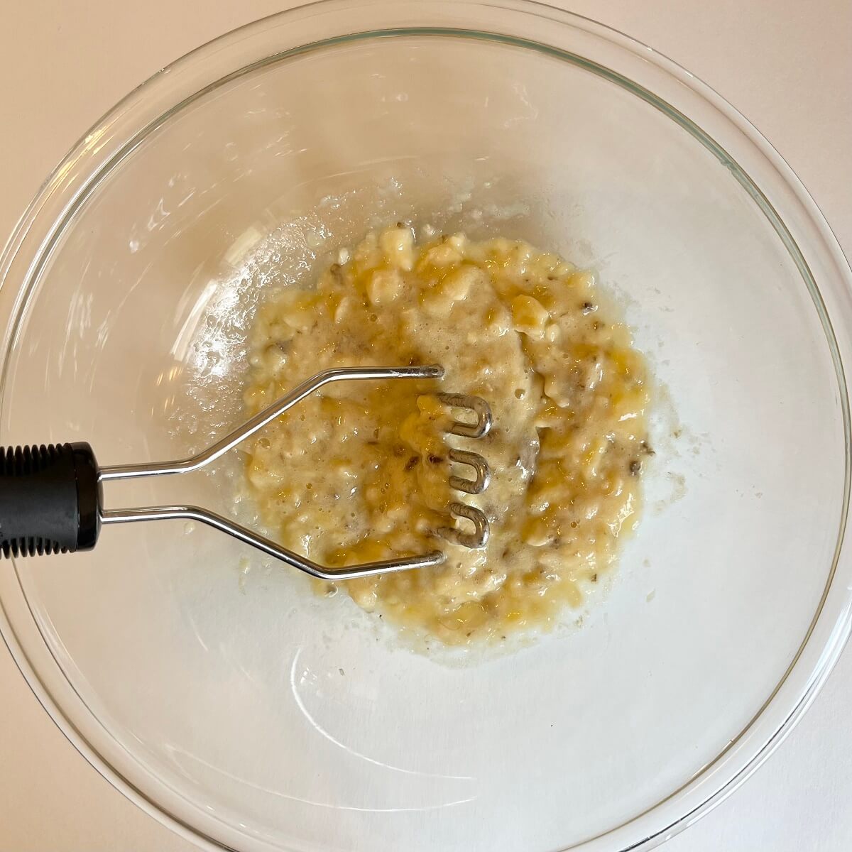 Bananas being mashed in a large glass mixing bowl.