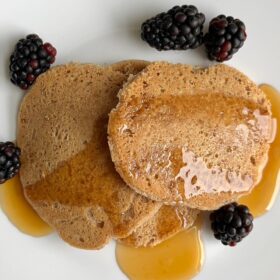 Pancakes on a white plate with berries and maple syrup.