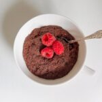 Paleo chocolate cake in a mug with three raspberries on top.